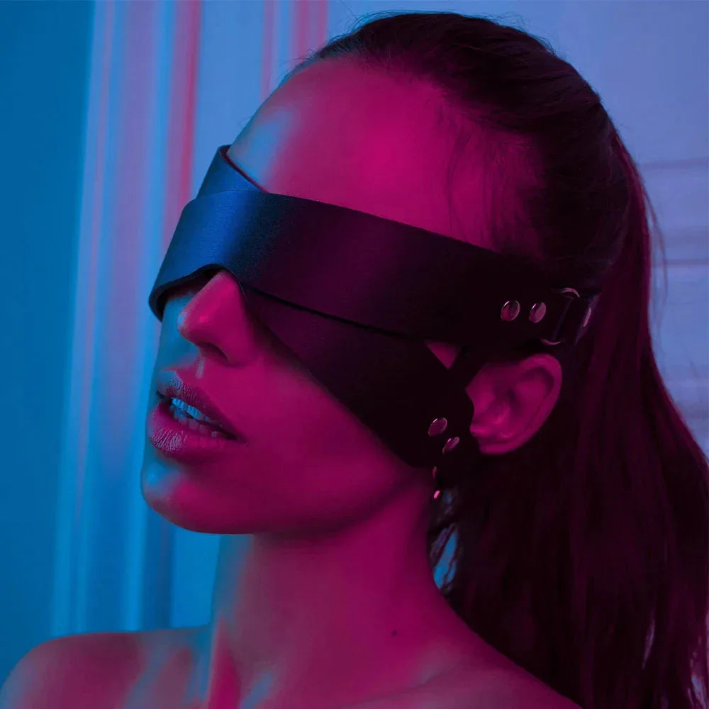 Woman wearing a black leather blindfold mask with adjustable straps in colorful lighting